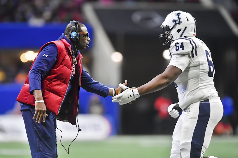 Coach wearing headphones congratulates football player in uniform.