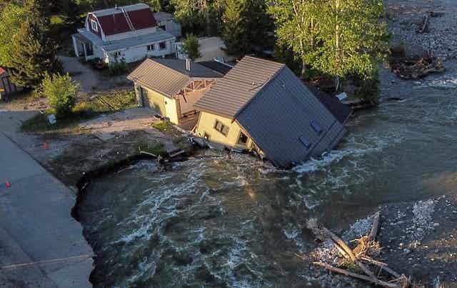 A house is tipped into the river after water cut a new channel beneath it. It also tore out a road and bridge.