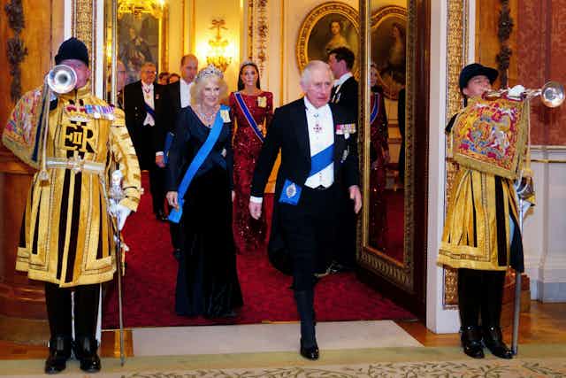 Charles and Camilla in formal wear with royal trumpeteers standing beside them