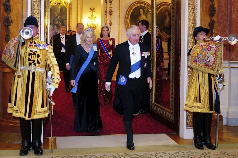 Charles and Camilla in formal wear with royal trumpeteers standing beside them
