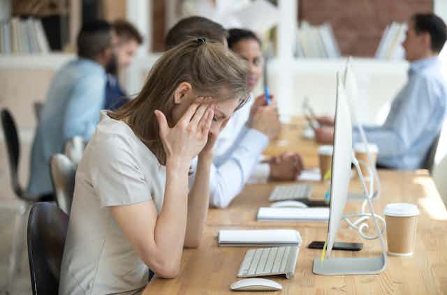 Mujer en la oficina con la cabeza entre las manos frente al ordenador.