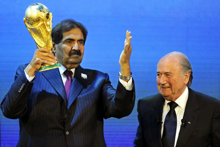 Emir of Qatar holds World Cup trophy next to Sepp Blatter.
