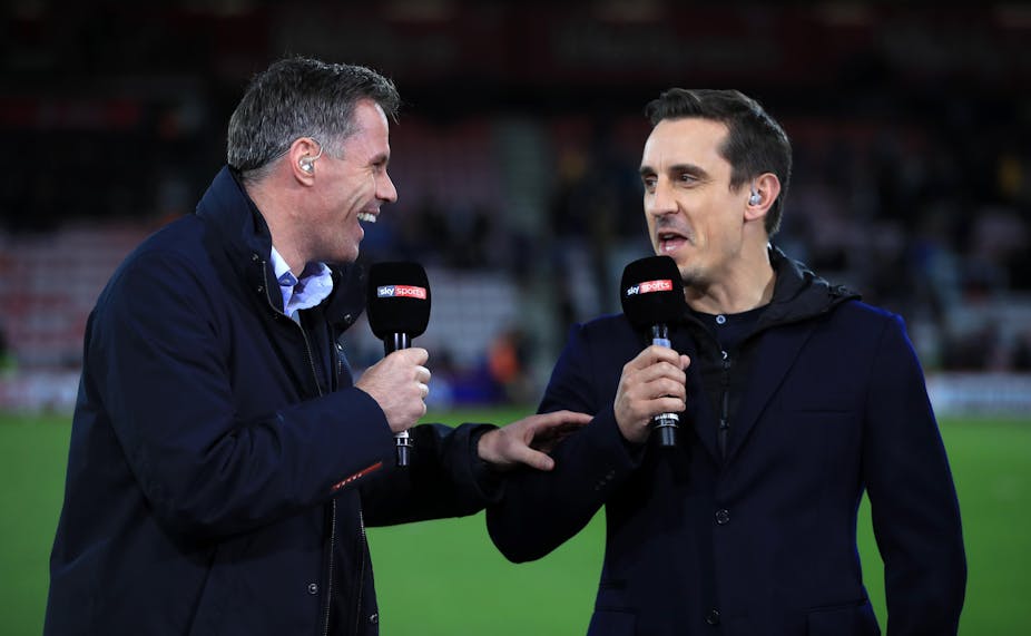 Two sports commentators speaking on a pitch. 