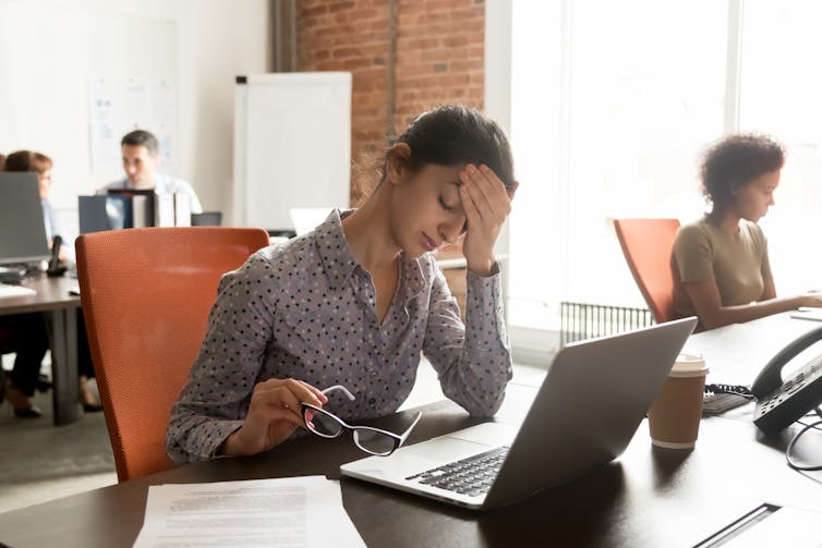 A woman with a cluster headache holds her head in pain while at her desk at work.