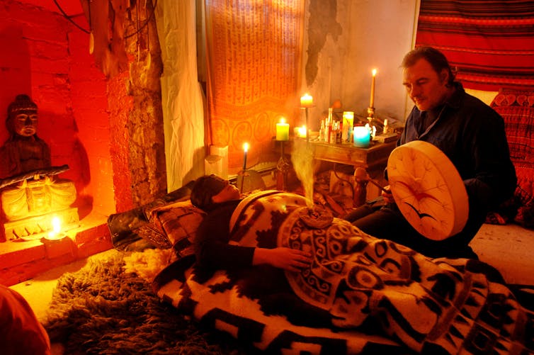 Shamanic practitioner treating a patient in therapy session by candlelight.