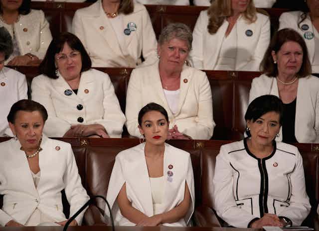 Three rows of women wearing white formal clothing are seated in formal looking seats.