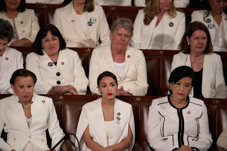Three rows of women wearing white formal clothing are seated in formal looking seats.
