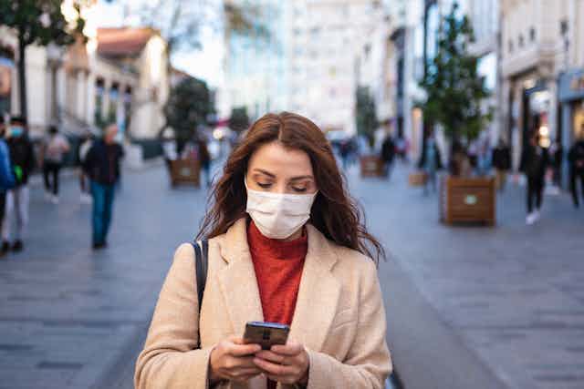 A woman wearing a mask looking at her phone.
