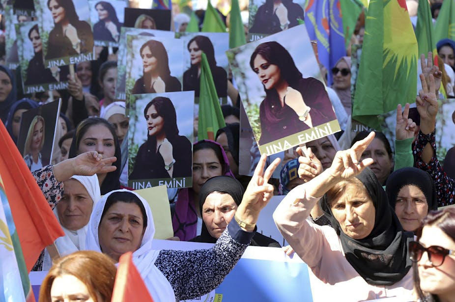 Women, with heads covered, holding up portraits of Iranian Mahsa Amini.