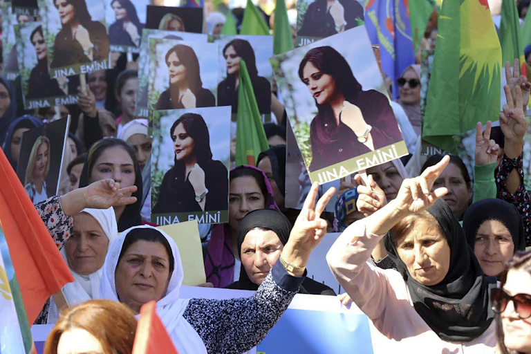Women, with heads covered, holding up portraits of Iranian Mahsa Amini.