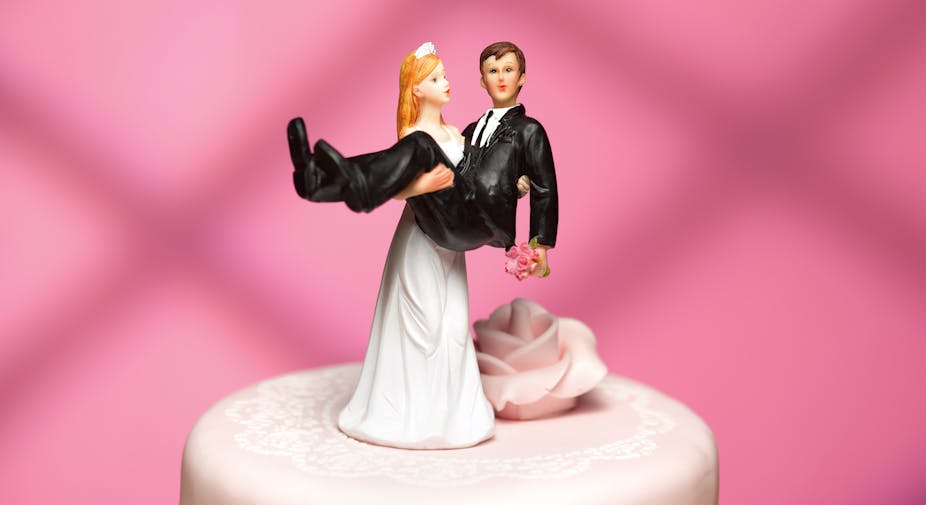 close up of bride cake topper carrying groom on top of light pink wedding cake