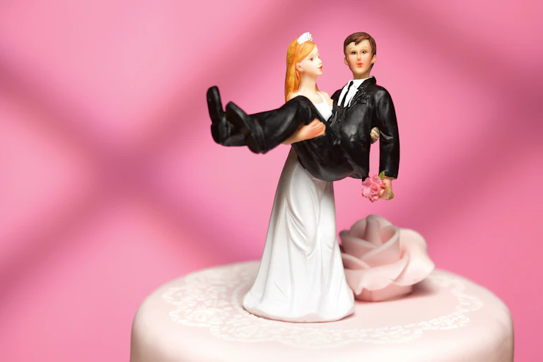 close up of bride cake topper carrying groom on top of light pink wedding cake