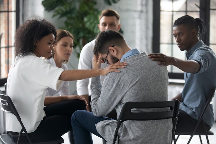 A man with his head in his hand is comforted by other people.