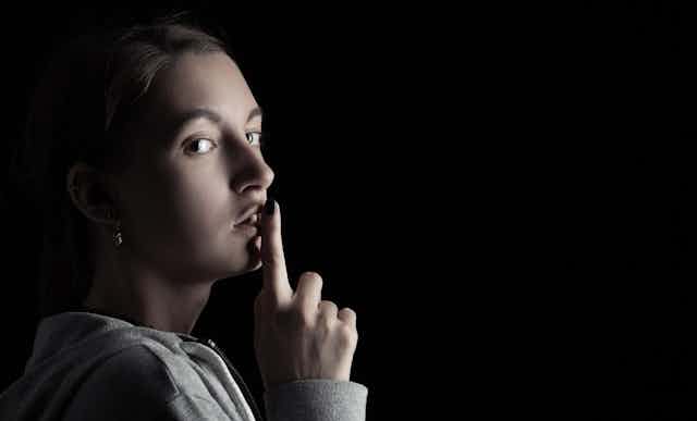 Young women makes a 'quiet' gesture with a finger against her lips.