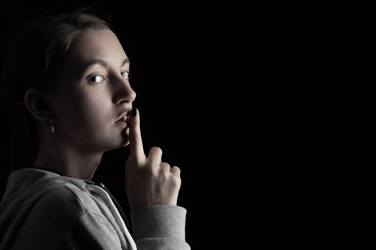 Young women makes a 'quiet' gesture with a finger against her lips.