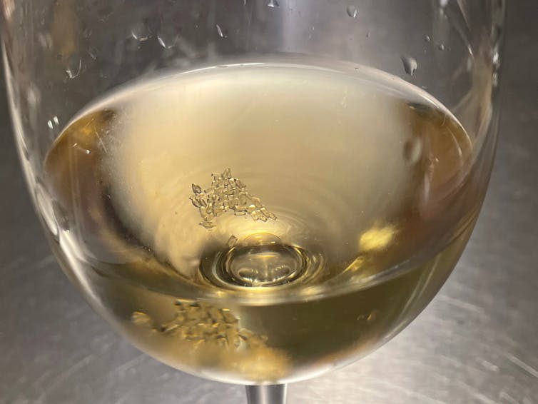 Tiny clear crystals ar‹e seen forming at the bottom of a glass of white wine.