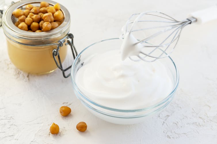 Chickpeas in a jar, next to a bowl of soft white peaks whipped from aquafaba.