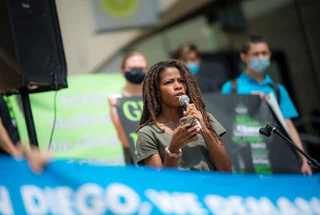 A student holds a micorphone during a rally with others behind her holding sights.