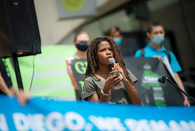 A student holds a micorphone during a rally with others behind her holding sights.
