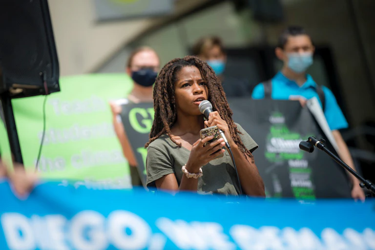A student holds a micorphone during a rally with others behind her holding sights.