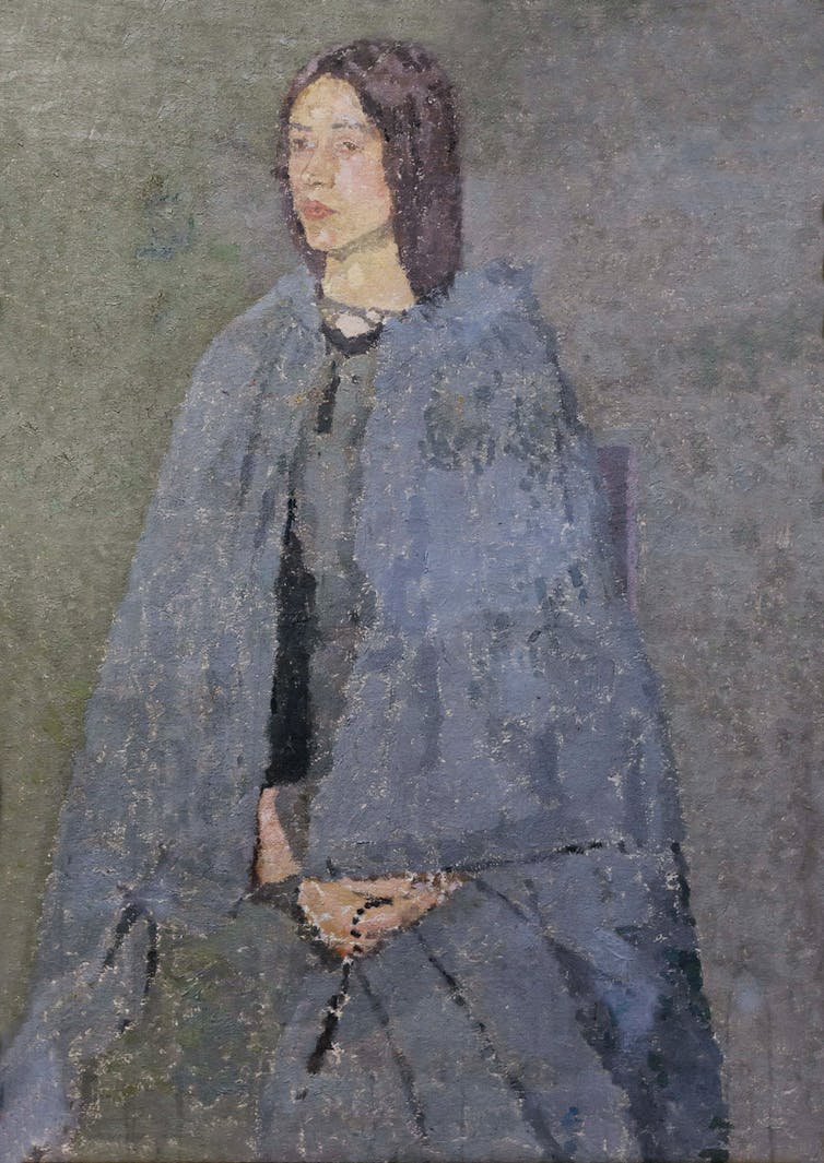 A woman seated wearing a large blue-grey cape.