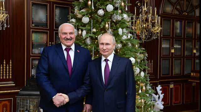Belarus president Alexander Lukashenko shakes hands with Russian president Vladimir Putin in front of a Christmas tree