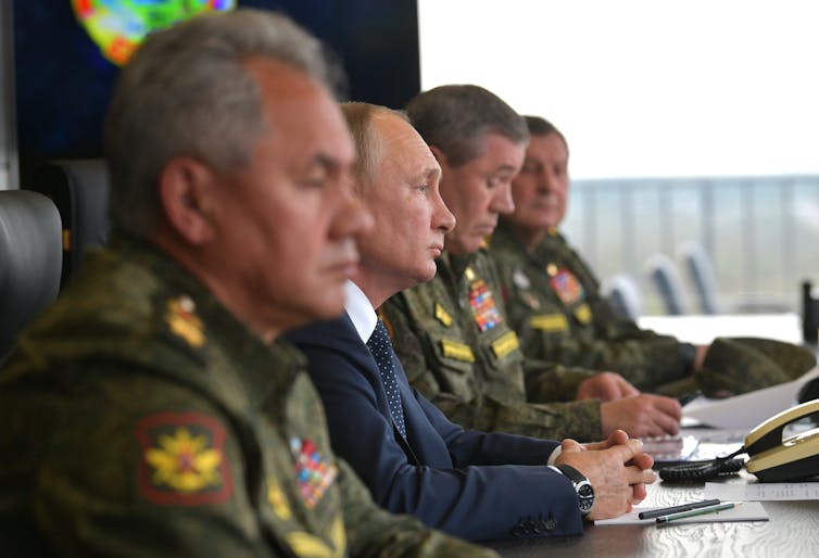 Russian defence minister Sergei Shoigu and Vladimir Putin sit at a desk with other Russian military officers.