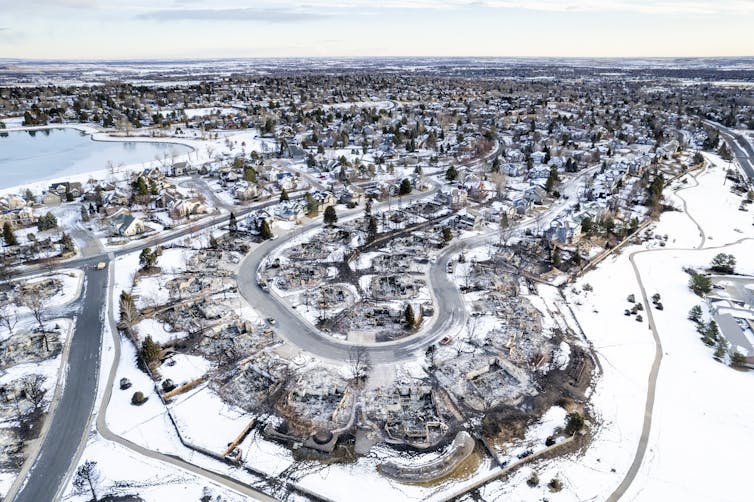 An aerial view of several streets with a lake in the background. Several homes are still standing among many others that were reduced to ashes.