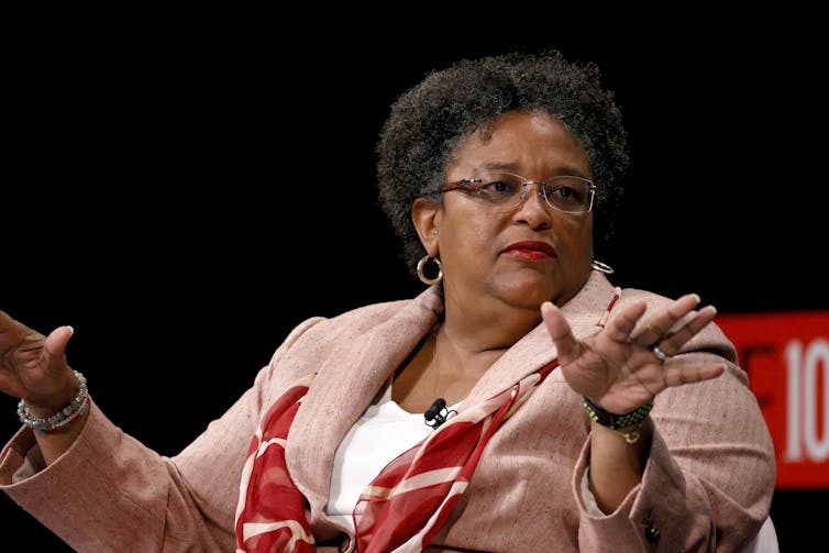 A woman sits on stage during an event and gestures with her hands.