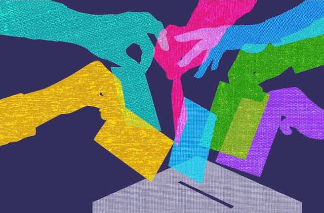 Multi-colored hands are seen putting colorful cards into a ballot boxx.