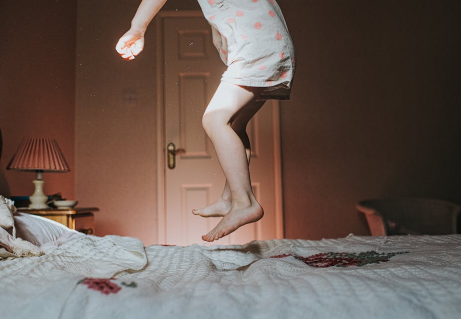child's torso and legs jumping on bed