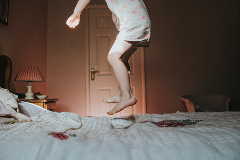 child's torso and legs jumping on bed