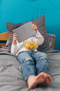 child lying in bed holding up tablet