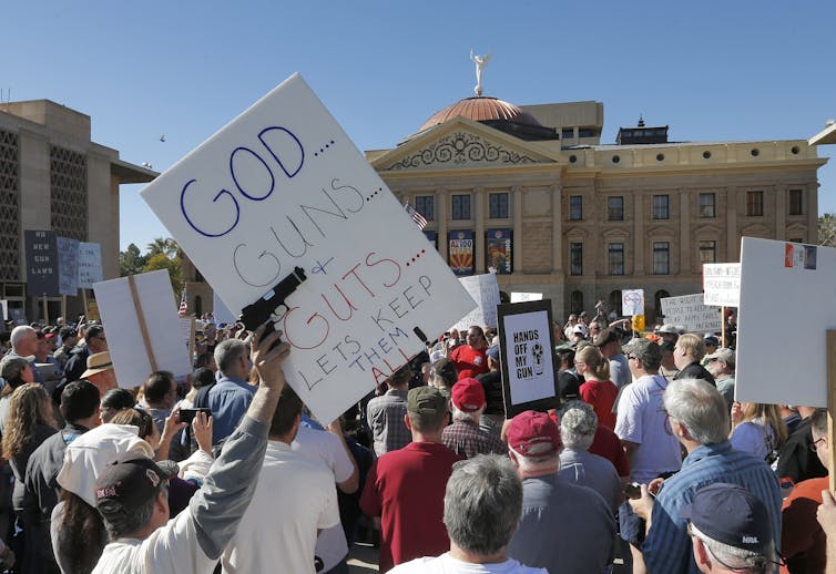 A crowd holds signs, including one that says, 'God...guns...and guts...lets keep them all.'