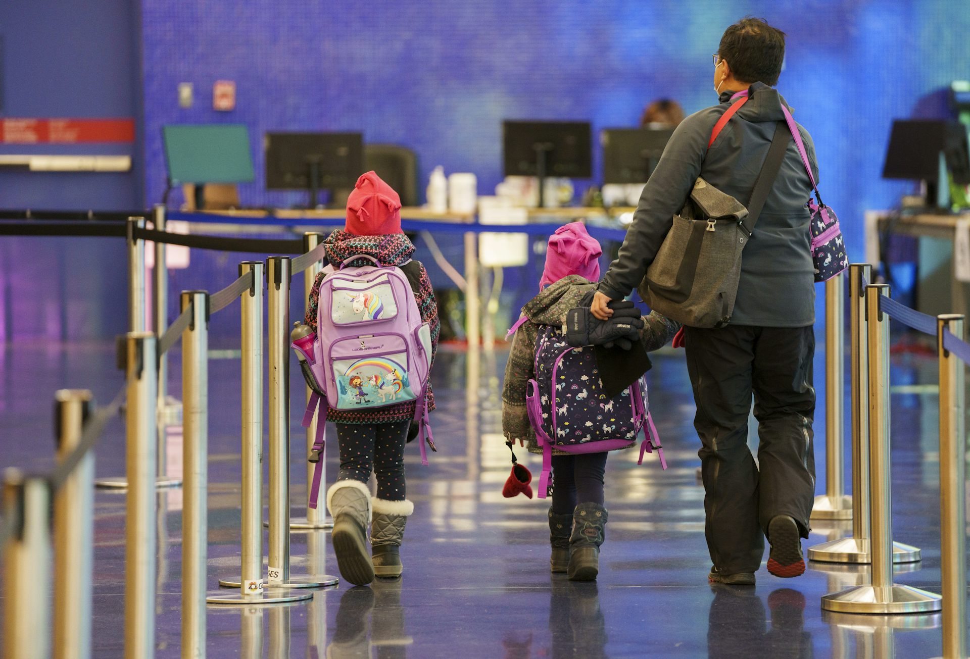 A man seen from behind with two children wearing bright pink hats and large backpacks.