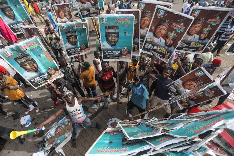 An overhead shows a group fo mainly men holding aloft placards.