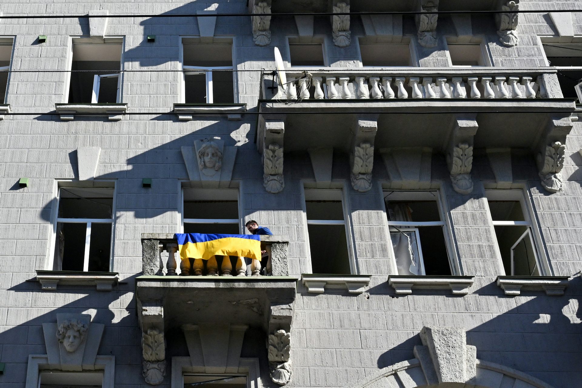 Un homme accroche un drapeau ukrainien sur le balcon d’un immeuble