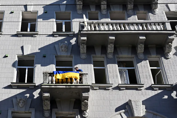 Un homme accroche un drapeau ukrainien sur le balcon d’un immeuble