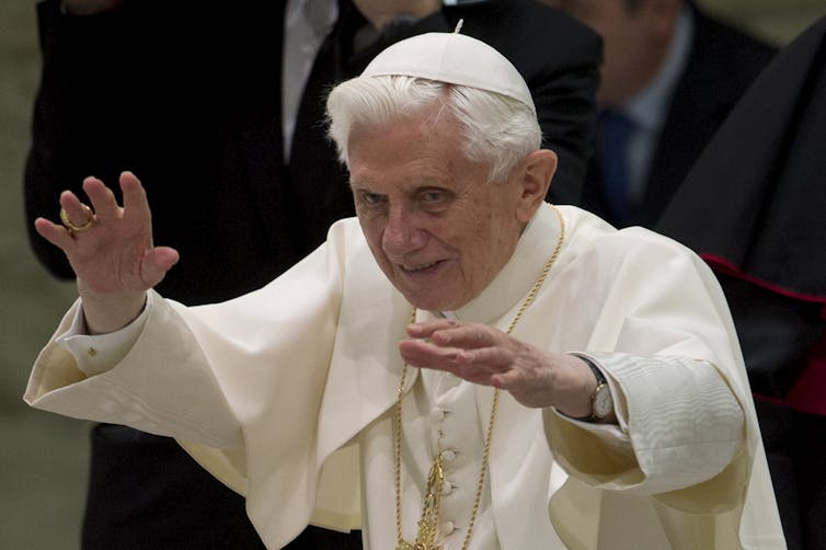 Pope Benedict XVI dressed in white robes raises both hands to greet people