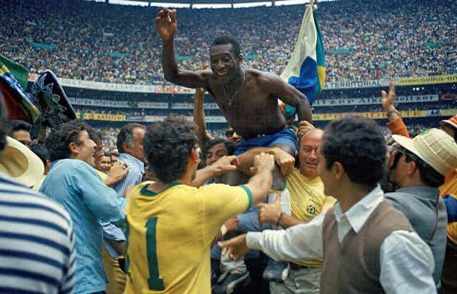 A bare-chested man is held aloft by others in the background in a full stadium of fans.