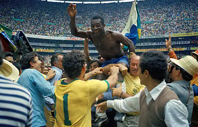 A bare-chested man is held aloft by others in the background in a full stadium of fans.
