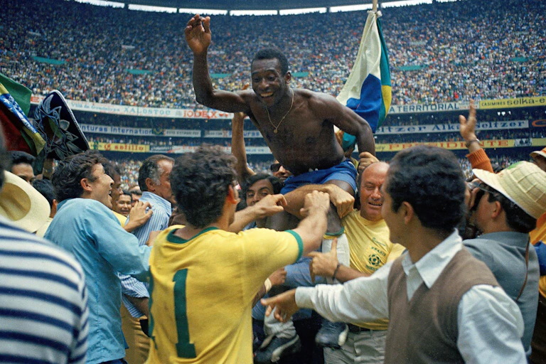 A bare-chested man is held aloft by others in the background in a full stadium of fans.