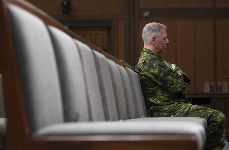 A man in camouflage clothing sits at the end of a row of seats.