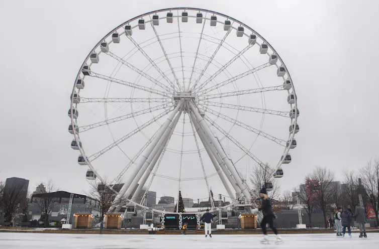 A ferris wheel seen behind people skating.