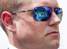 A woman is reflected in a man's sunglasses.