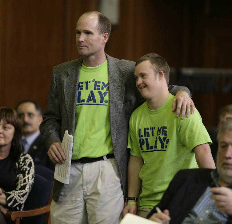 A father and son seen standing in shirts that say 'Let him play' and 'Let me play.'