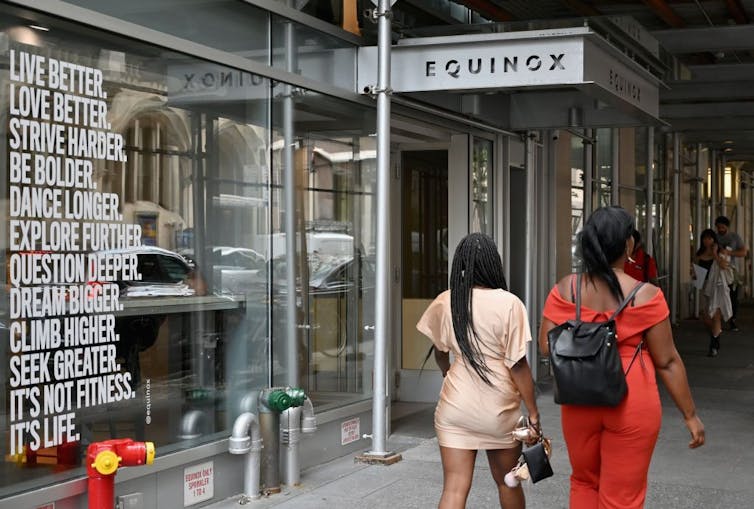 Two women walk by a storefront with inspirational messaging on the wall.