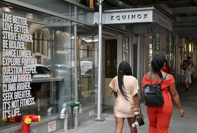 Two women walk by a storefront with inspirational messaging on the wall.