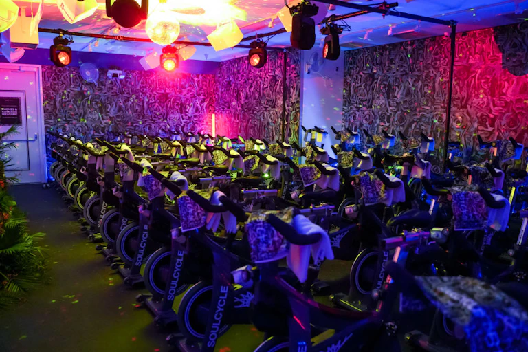 A roomful of close-spaced bikes, with purple, pink and blue lights on the walls.