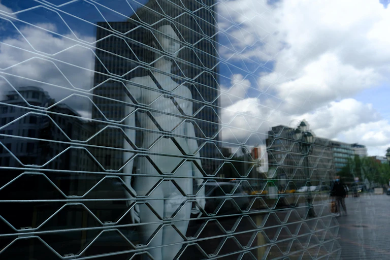 Un maniquí desnudo en un escaparate tras unas rejas.